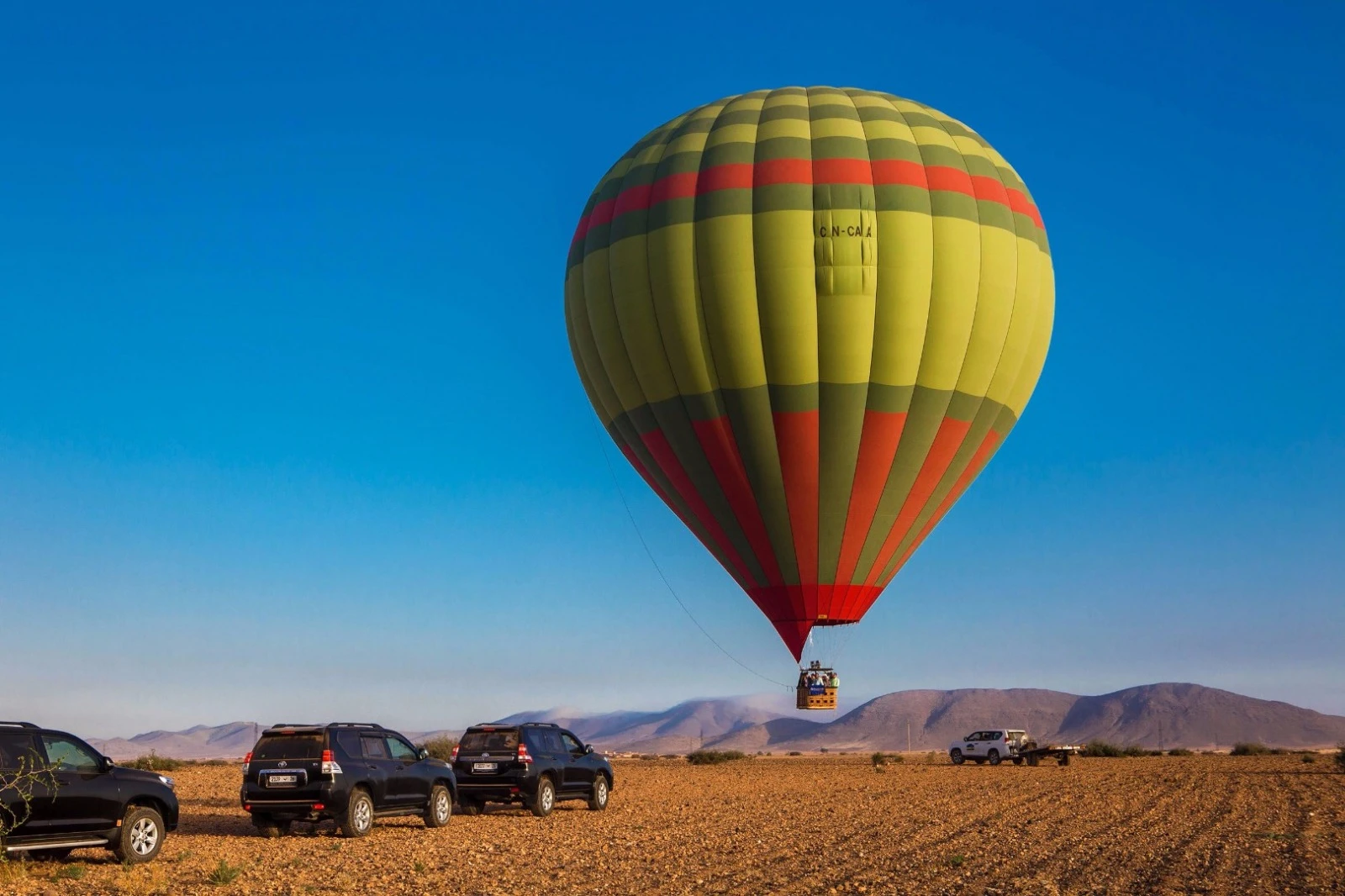 Montgolfière jaune-vert dans un ciel bleu intense avec escorte 4×4