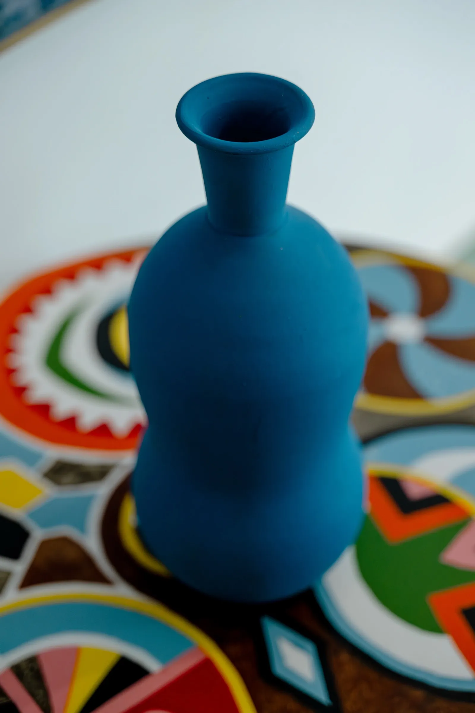 Vase bleu mat sur table aux motifs colorés